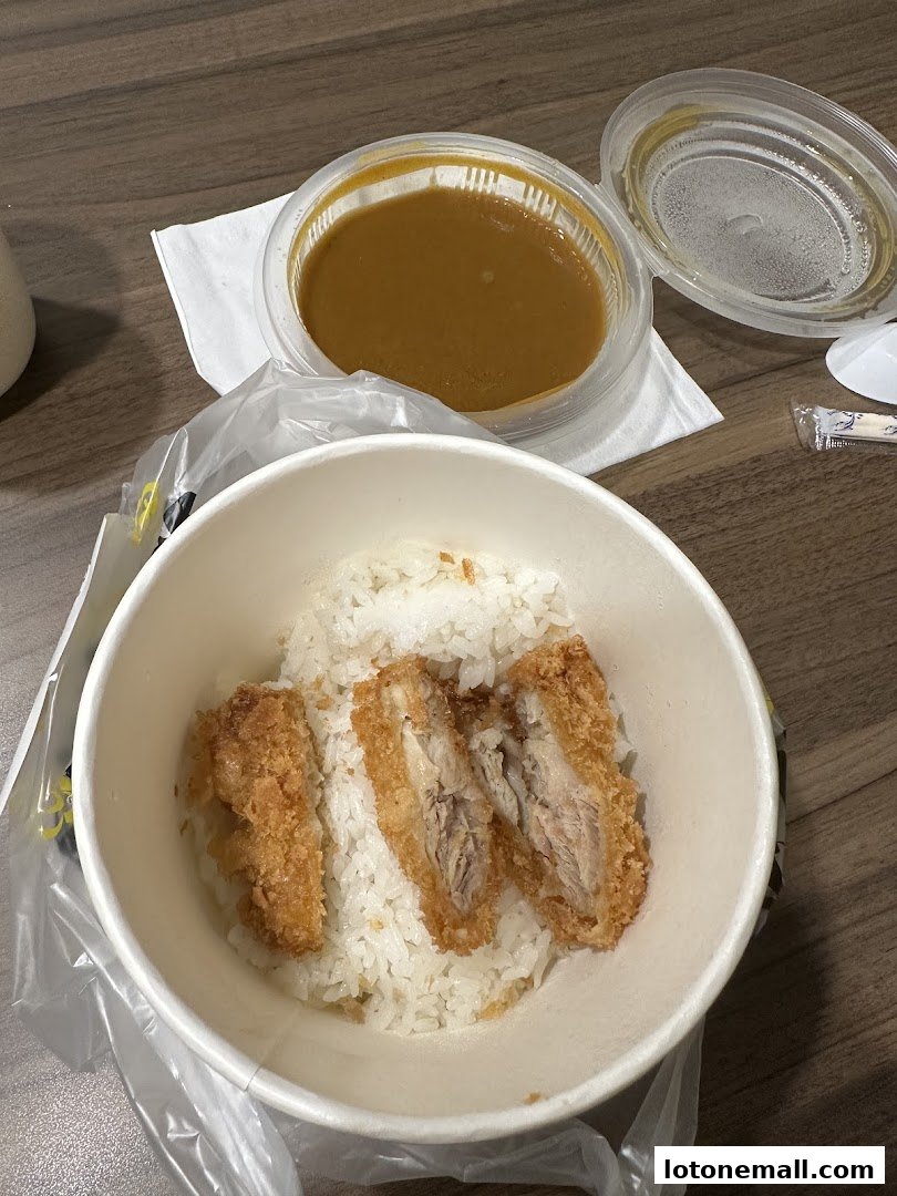 A bowl of rice topped with three pieces of crispy fried chicken and a side of curry sauce.