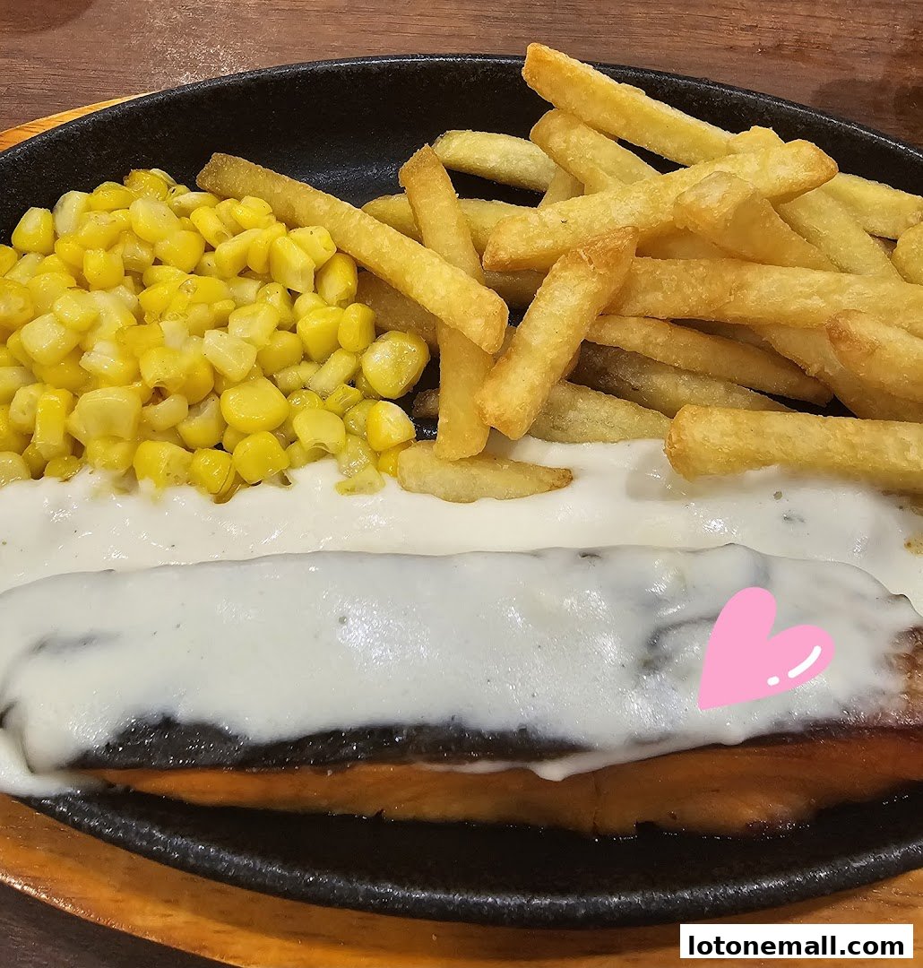 A close-up of a sizzling steak dish with fries and corn, topped with creamy sauce.