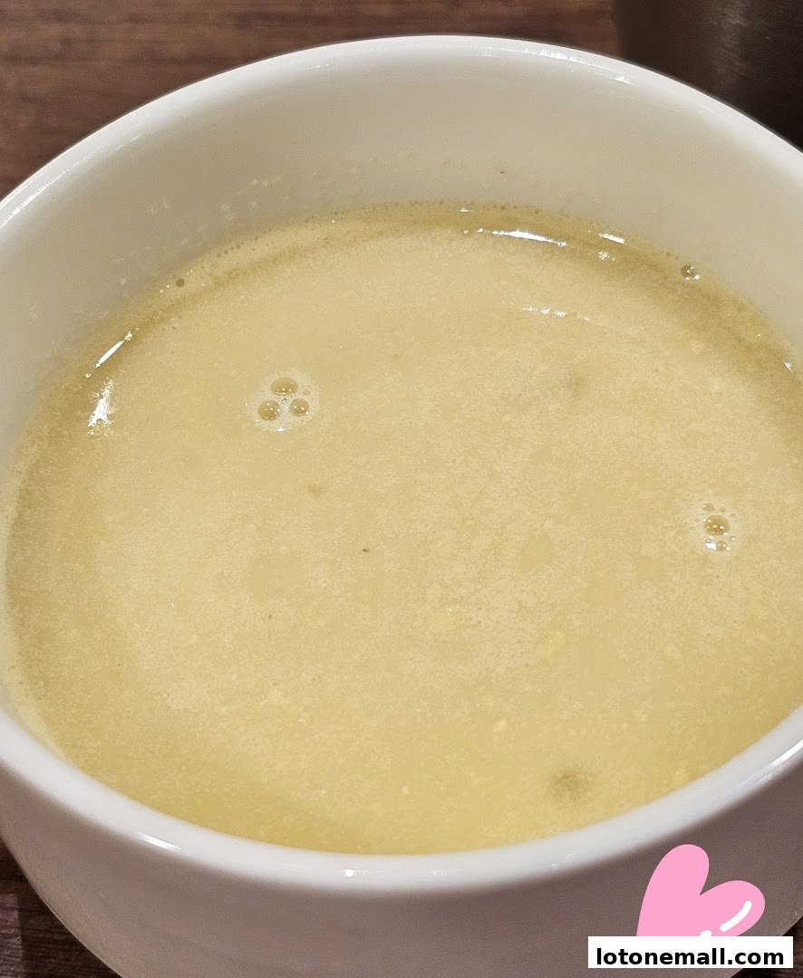 A close-up shot of a bowl of creamy, light yellow soup with small bubbles.