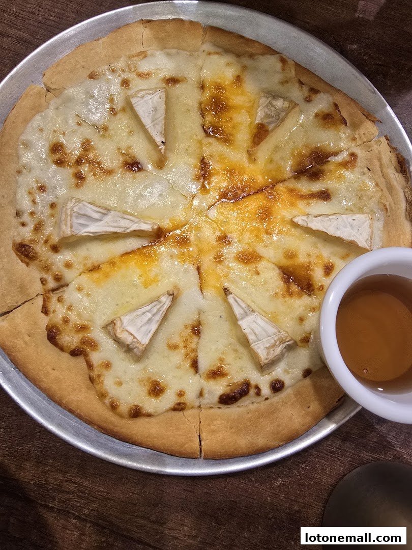 A delicious cheese pizza with wedges of brie and a side of honey.