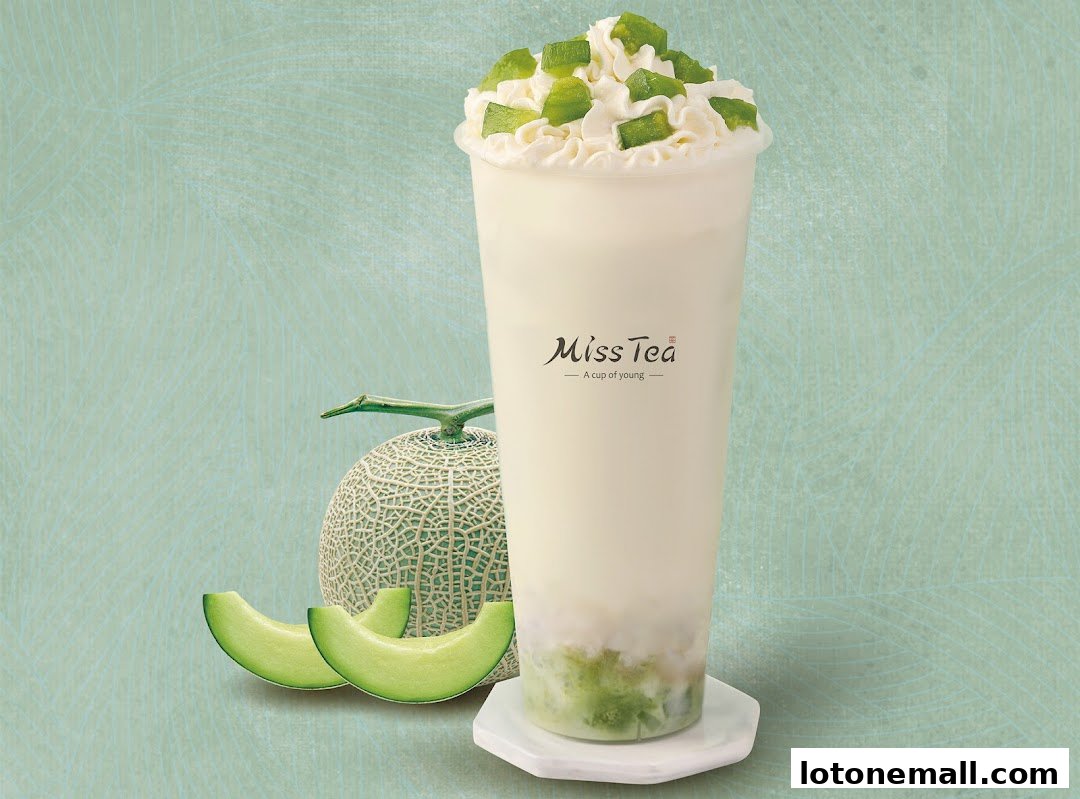 A tall cup of creamy beverage topped with whipped cream and green cubes, next to a cantaloupe and slices.