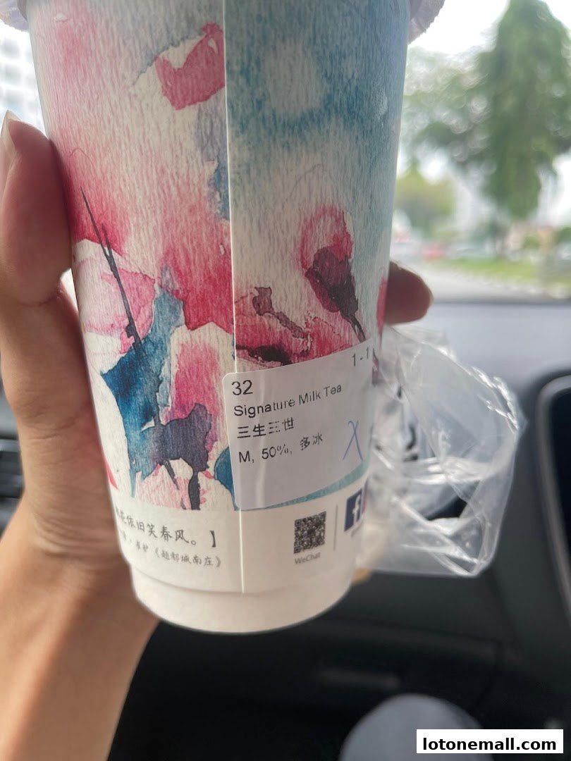 A hand holds a cup of Signature Milk Tea with floral designs and order details.