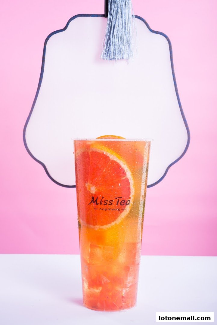 A refreshing grapefruit tea with fresh fruit slices and ice, presented against a pink background.