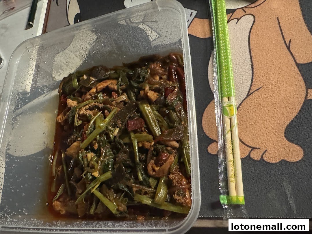 A clear plastic container filled with stir-fried vegetables and meat, next to chopsticks.