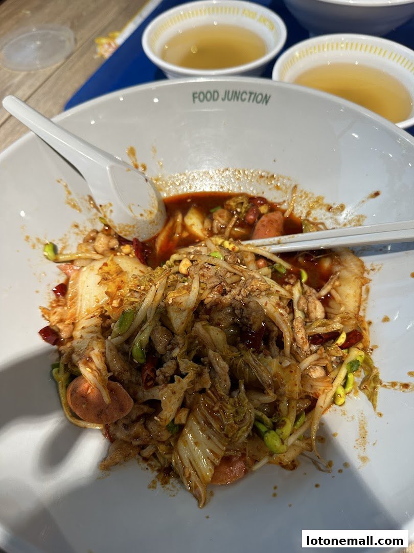 A bowl of spicy noodles with vegetables and meat, served with two small bowls of broth.