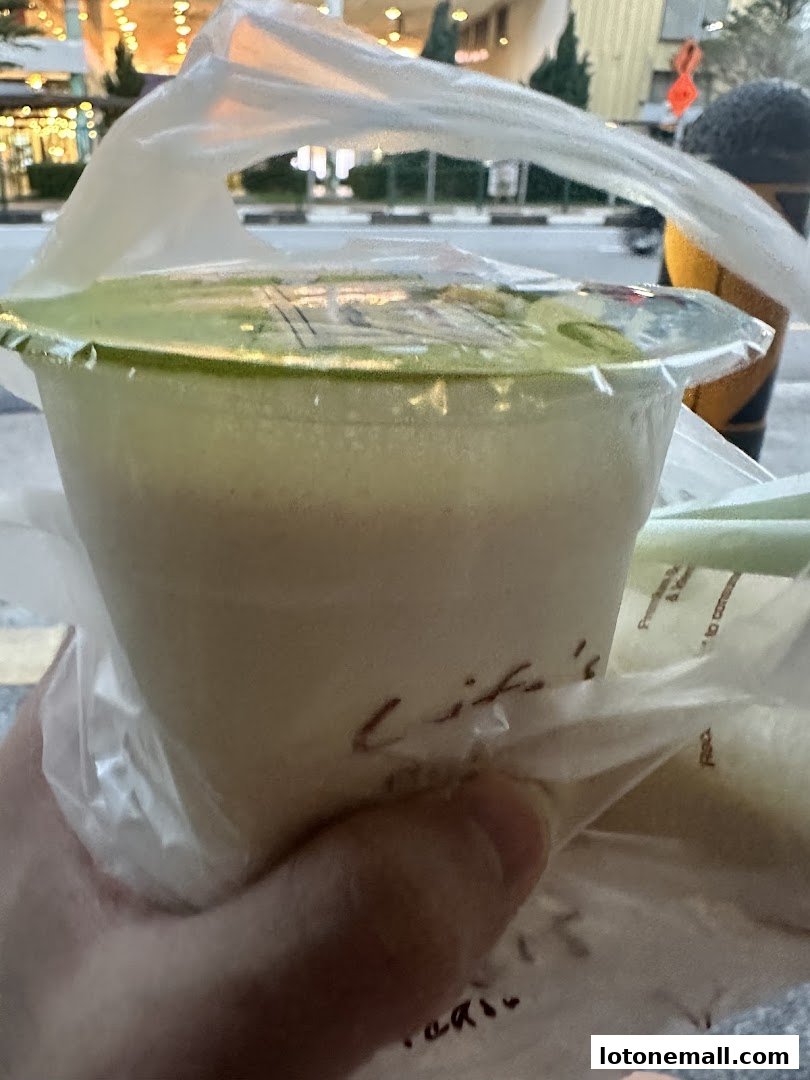 A hand holds a plastic-wrapped drink with a green lid and straw.