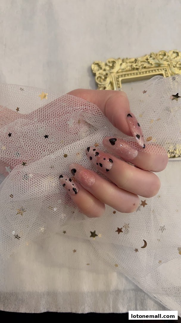 A hand with long, elegant nails adorned with a pink glitter base and black heart designs.