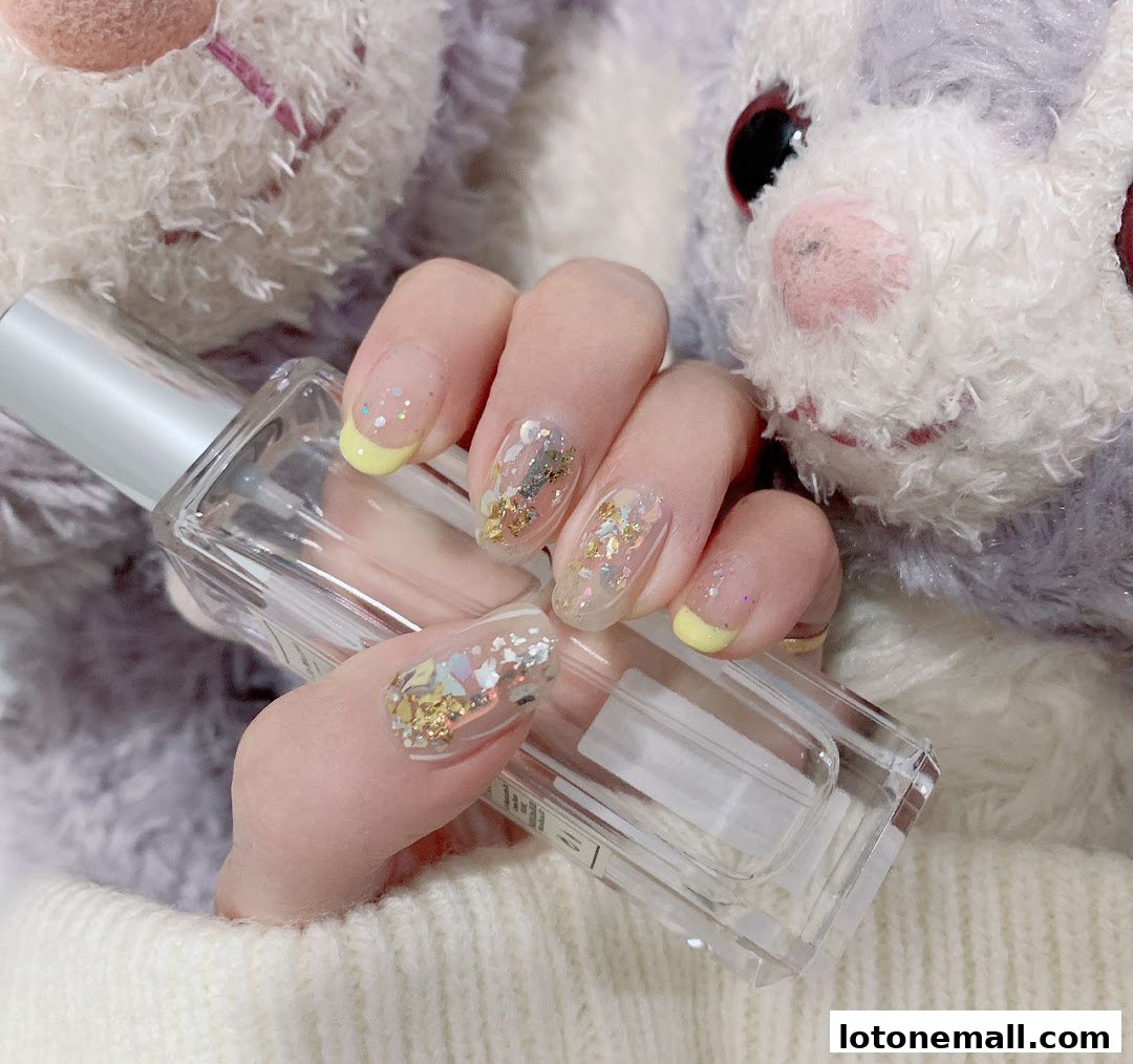 A hand with beautifully decorated nails holding a clear bottle, with a plush toy in the background.
