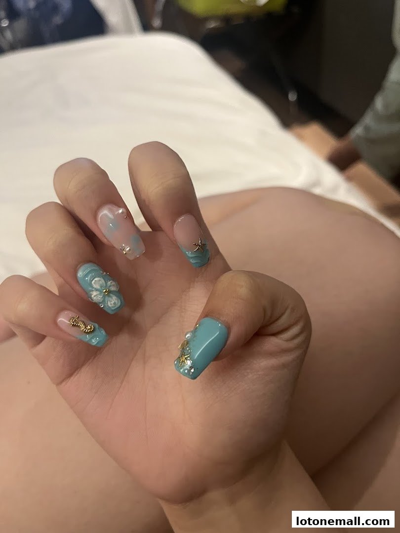 A close-up of a hand with beautifully decorated turquoise and clear nails featuring floral and starfish designs.