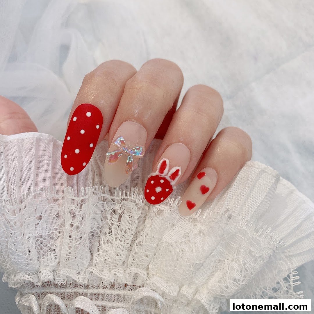 A close-up of a hand with intricately designed nails featuring red and white polka dots, a bunny, and hearts.