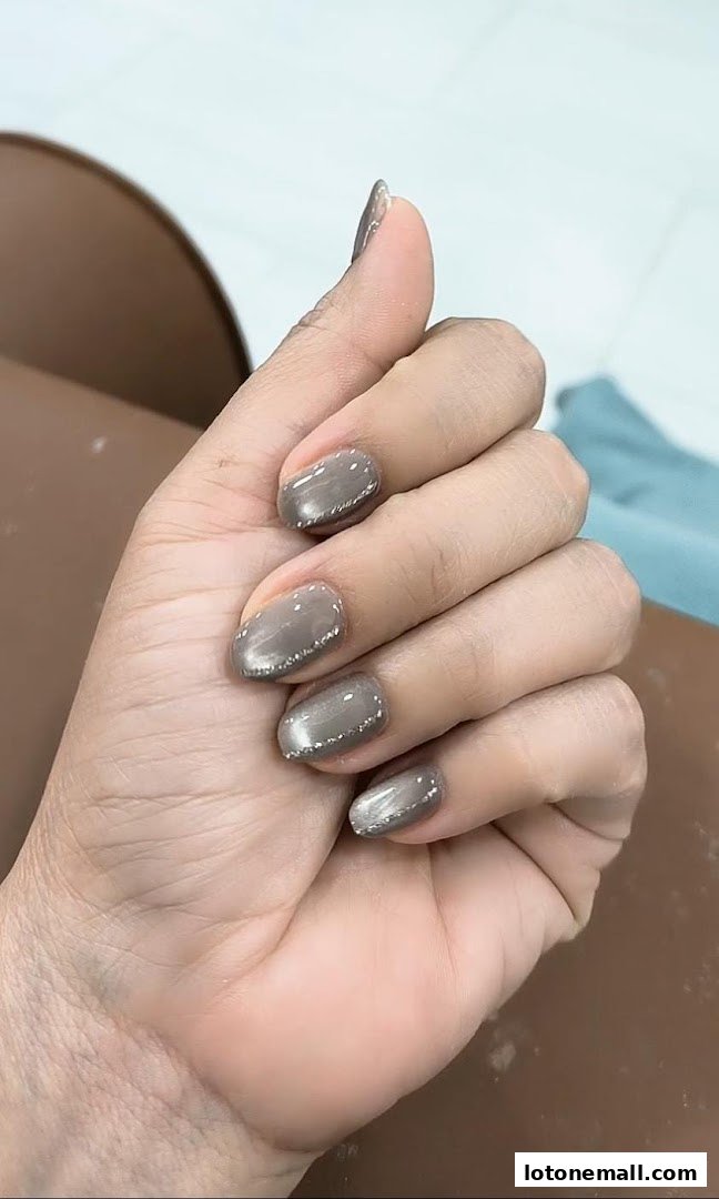 A close-up of a hand with beautifully manicured nails featuring a grey polish and subtle glitter accents.