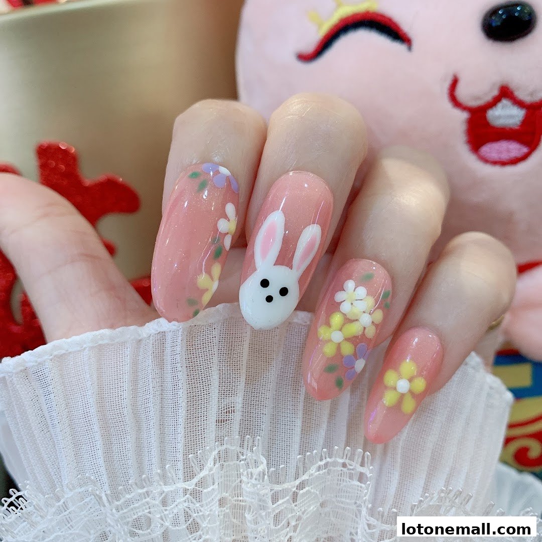 Close-up of a hand with pink gel nails featuring a bunny and floral designs.