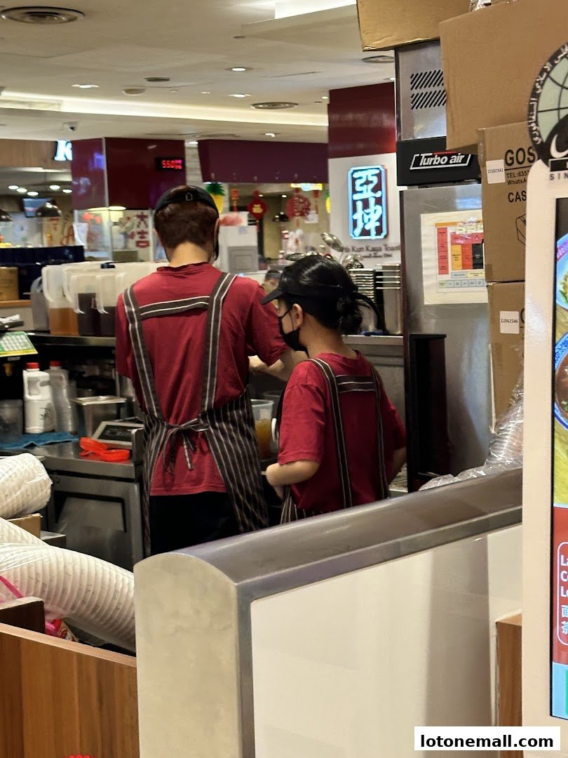 Two staff members in red uniforms and aprons preparing drinks behind a counter.