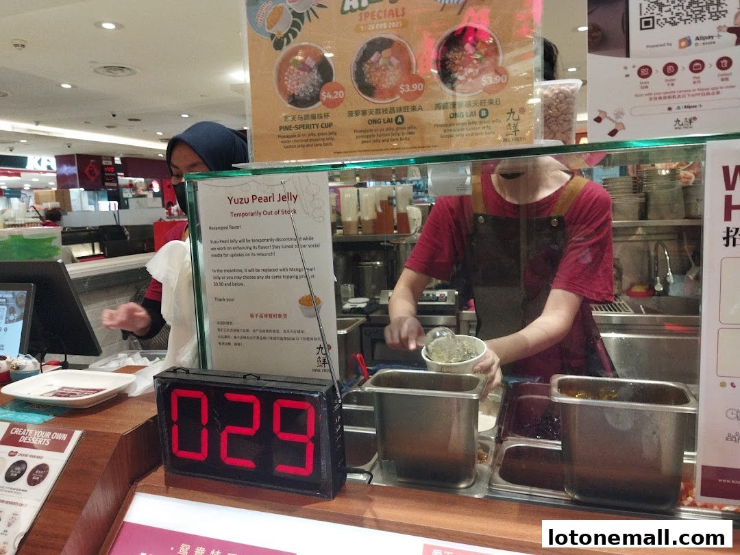 A dessert shop counter with staff preparing orders and a sign indicating an item is out of stock.