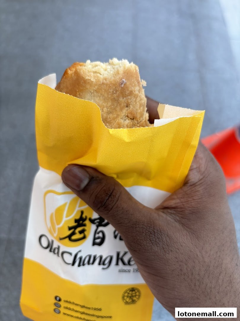 A hand holds a piece of fried food in a yellow Old Chang Kee paper bag.