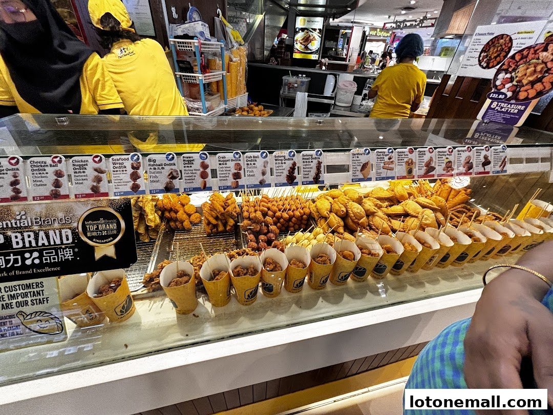 A display of various fried snacks and skewers at a food stall, with staff in the background.