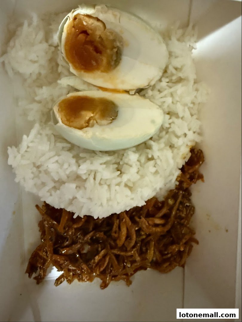 A close-up of a meal featuring rice, salted egg halves, and stir-fried anchovies.