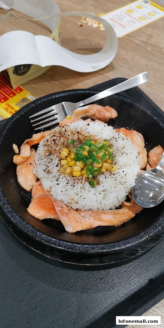 A sizzling plate of salmon with rice, corn, and green onions, served with cutlery.