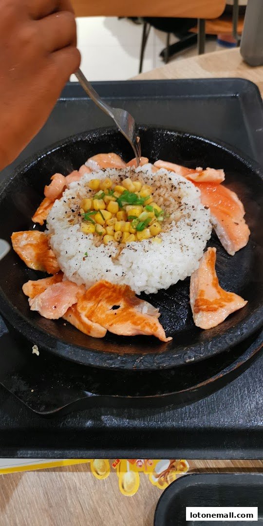 A sizzling plate of rice with salmon and corn, being eaten with a fork.