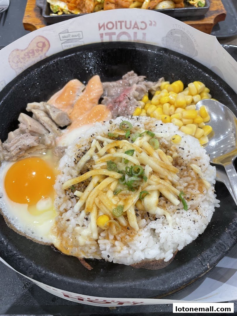 A sizzling hot plate meal with rice, salmon, beef, egg, corn, and cheese.