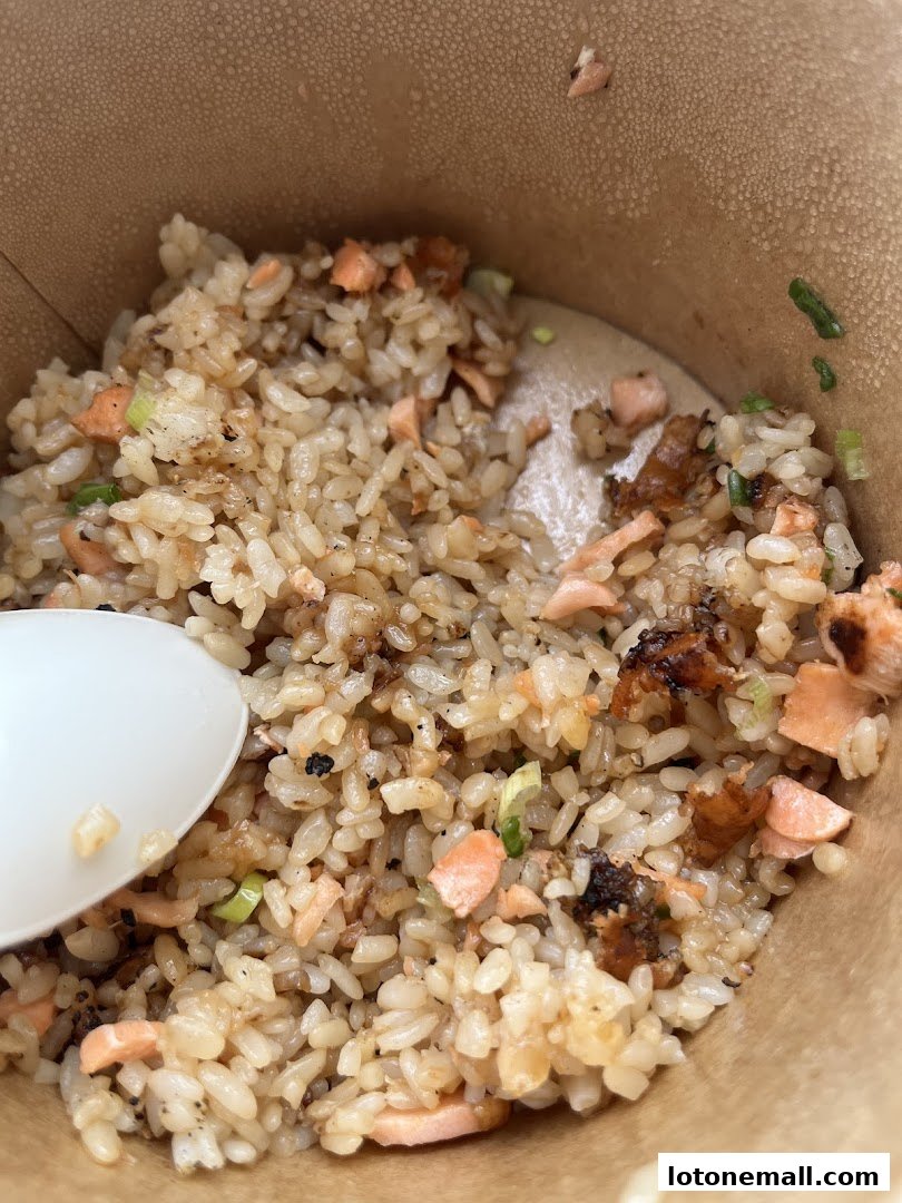 A close-up of a bowl of salmon fried rice with a spoon.