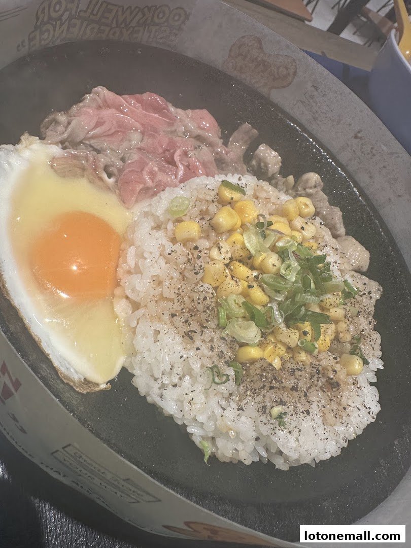 A sizzling hot plate meal with rice, fried egg, beef, and corn.