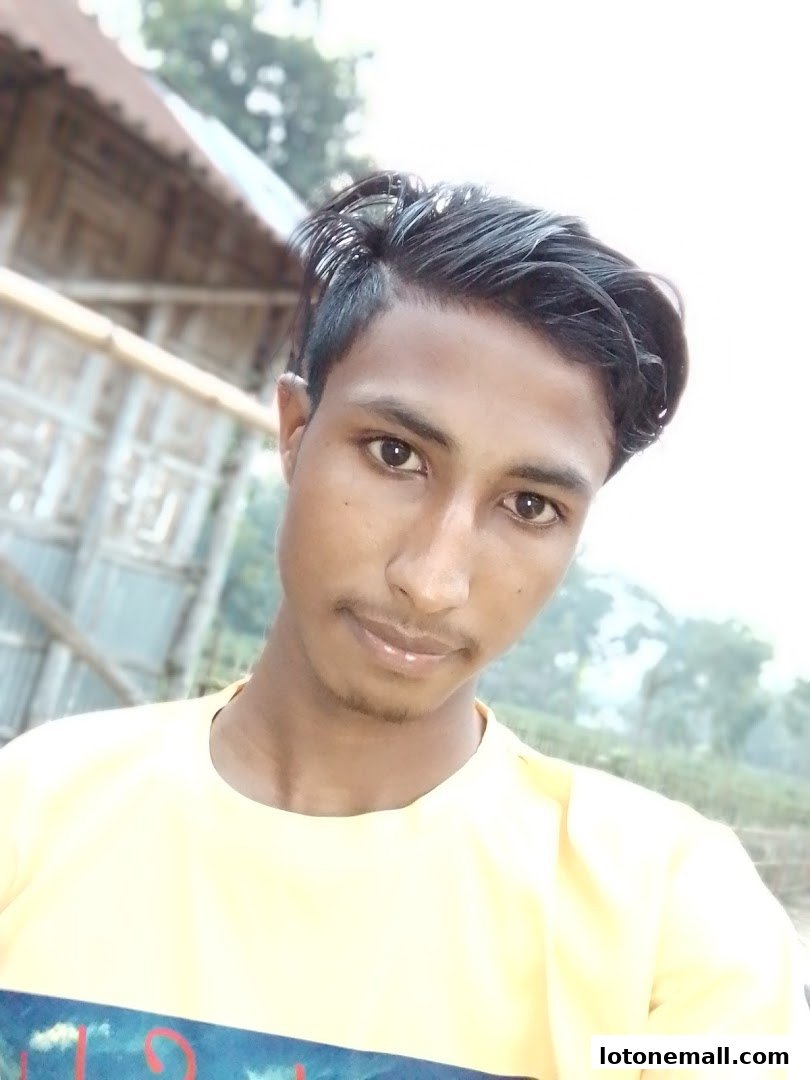 A young man with styled hair and a yellow t-shirt poses for a selfie outdoors.