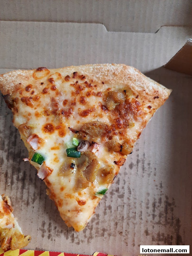A slice of pizza with cheese, meat, and vegetables in a pizza box.