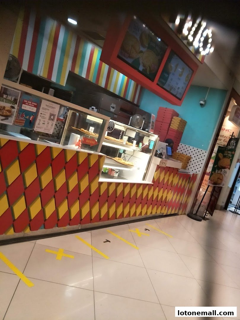 A colorful pizza shop counter with a digital menu board and queue markings on the floor.