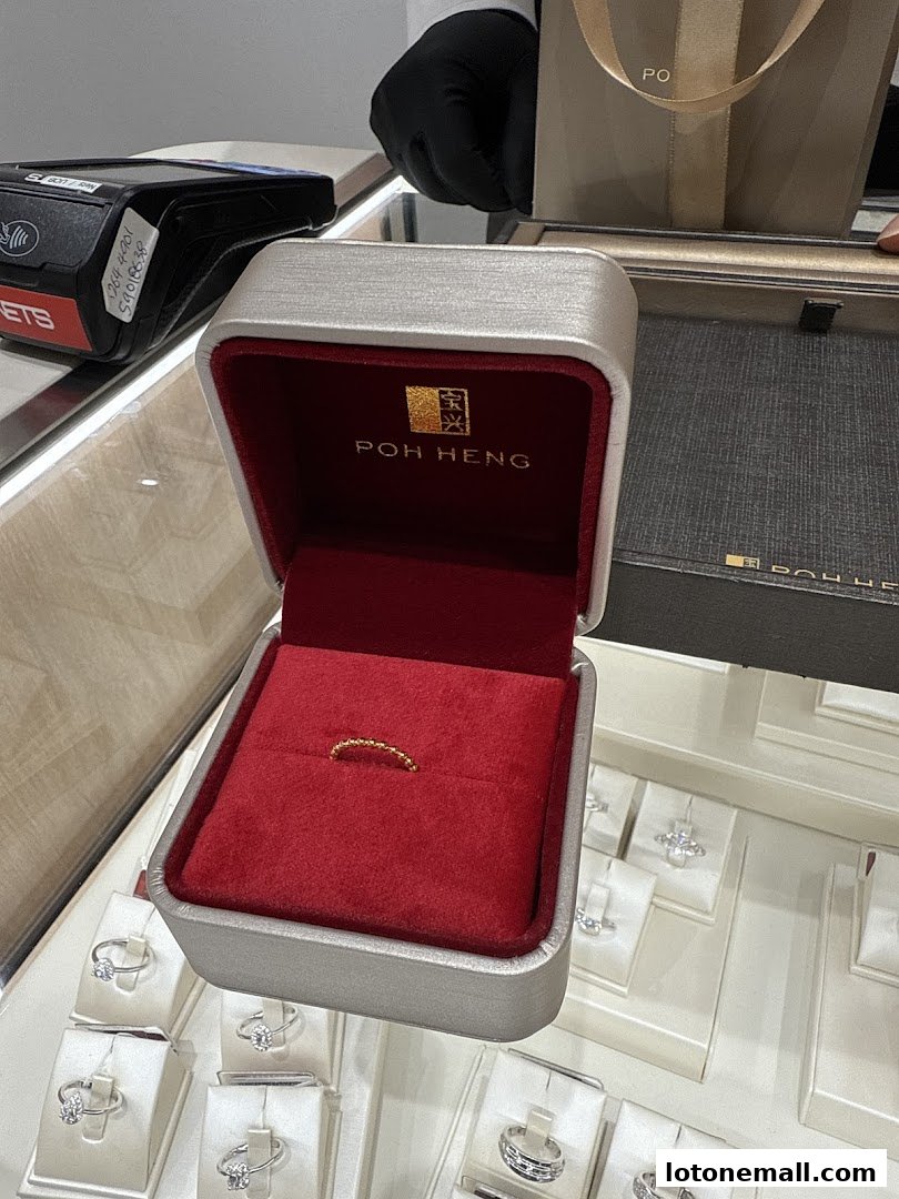 A gold beaded ring is displayed in an open jewelry box, with other rings visible in display cases.