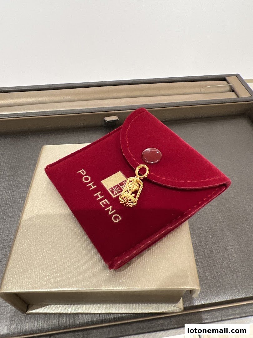 A gold pendant is displayed on a red velvet pouch with the Poh Heng logo.