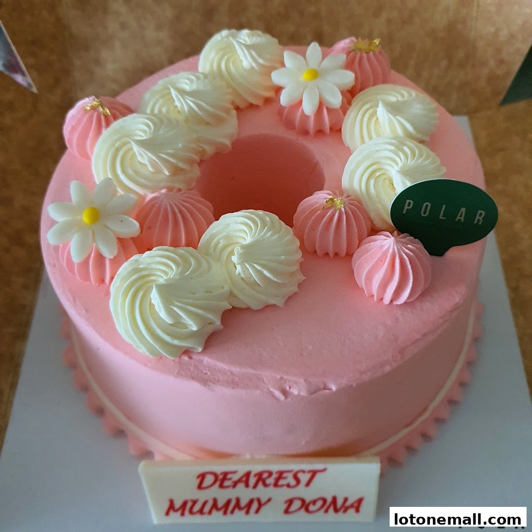 A beautifully decorated pink cake with white and pink frosting swirls and flower decorations.