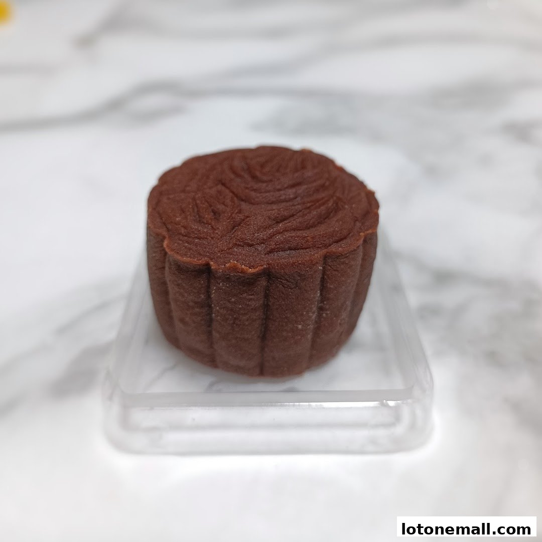 A close-up shot of a single chocolate mooncake on a clear plastic tray.