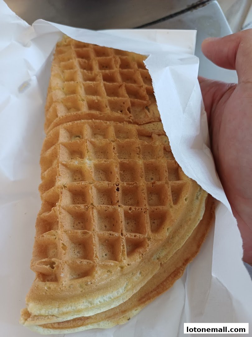 A hand holding a stack of freshly baked golden brown waffles wrapped in white paper.