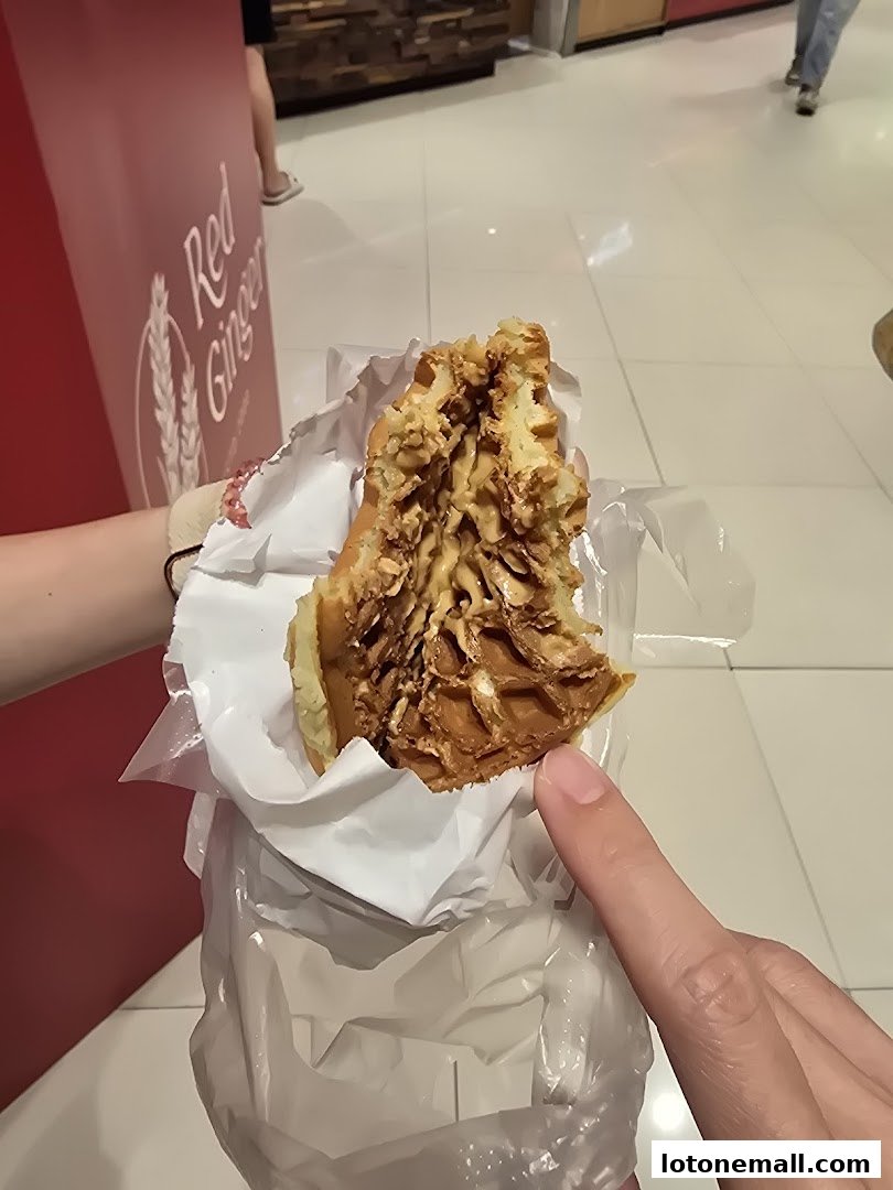 A person holds a half-eaten waffle with peanut filling, with a red wall in the background.