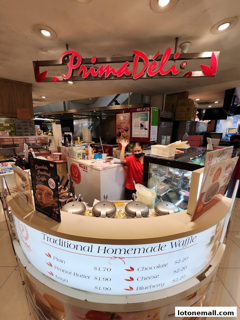 A PrimaDéli counter with a staff member waving, showcasing traditional homemade waffles and various toppings.