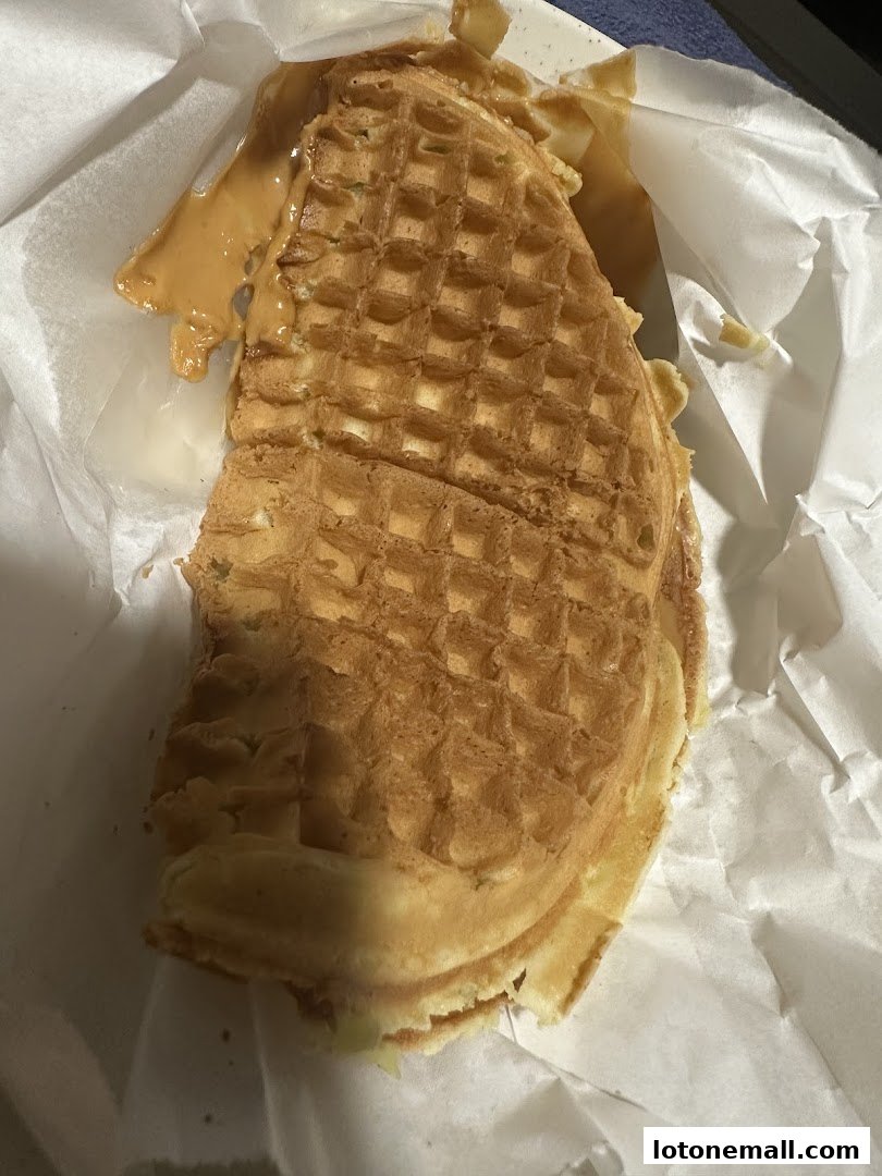 A close-up of a golden-brown waffle with peanut butter filling, wrapped in white paper.