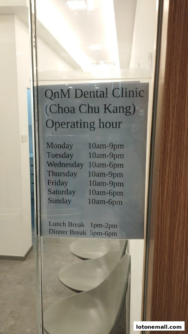 A sign on a glass door displays the operating hours for QnM Dental Clinic in Choa Chu Kang.