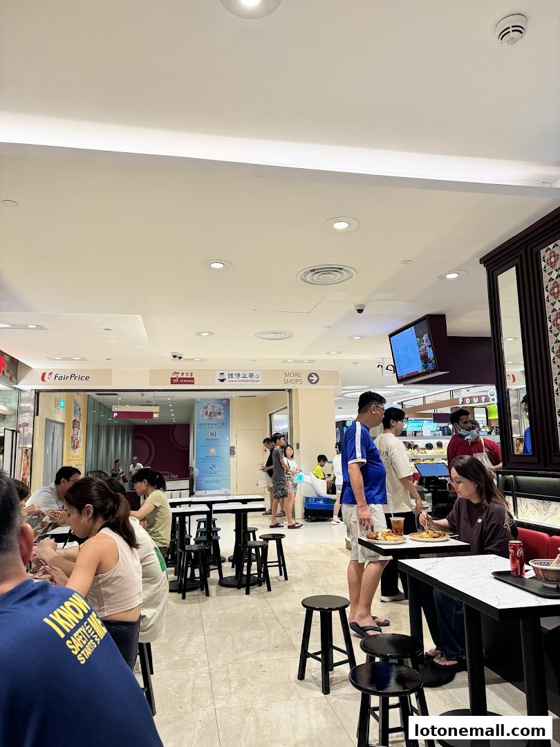 People dining at tables inside a brightly lit food court with various shops visible.