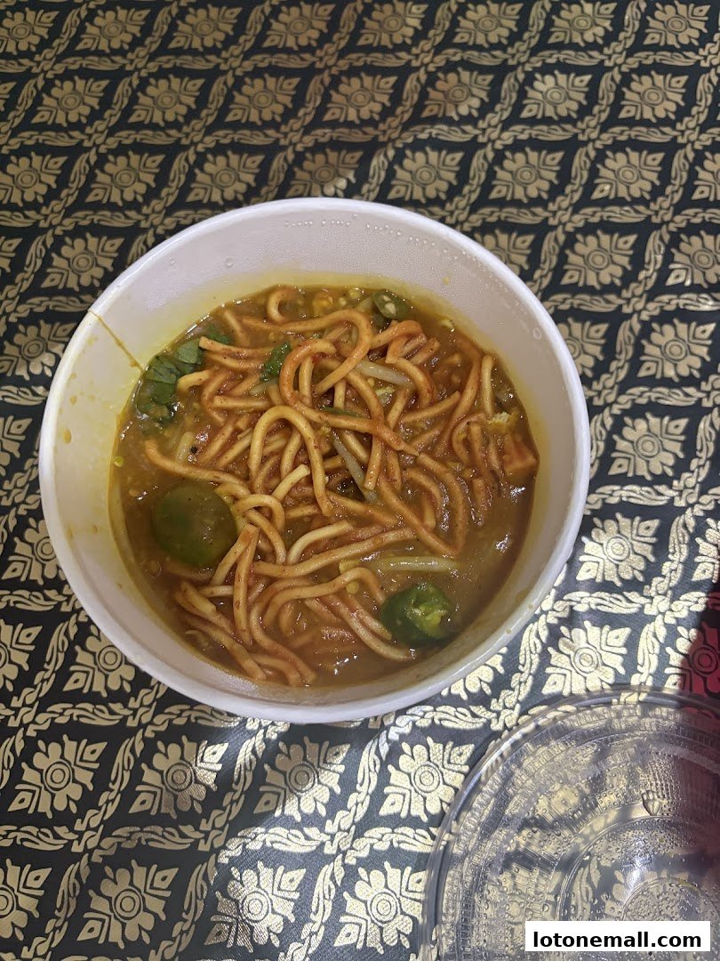 A bowl of noodles with broth and green chili slices on a patterned cloth.