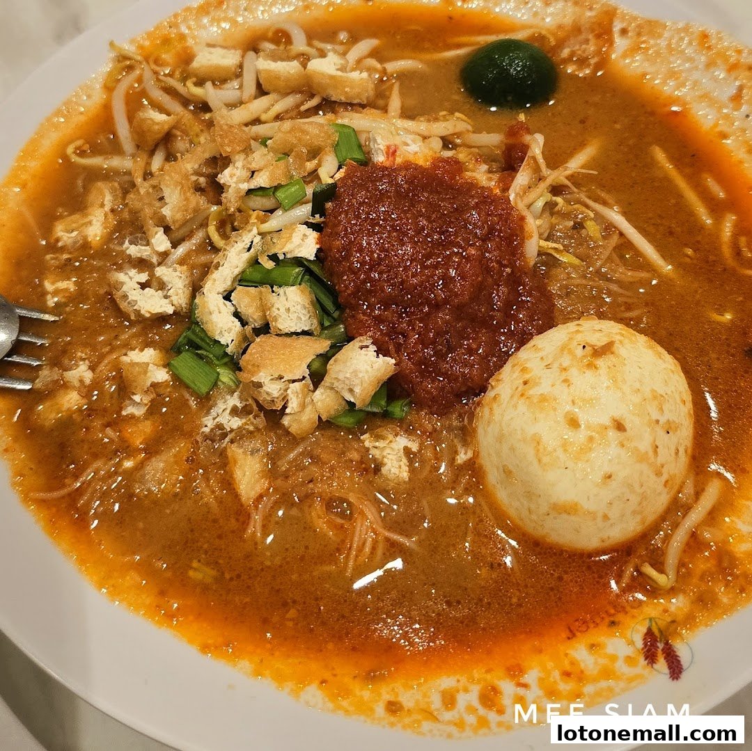 A close-up shot of a delicious bowl of Mee Siam with a side of chili paste and a fish ball.