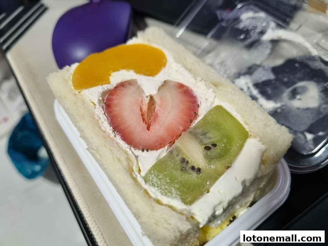 A fruit sandwich with cream, strawberry, kiwi, and peach slices on white bread.