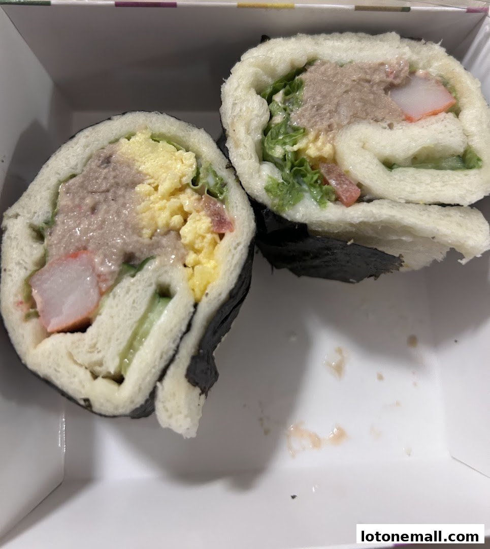 Two halves of a sushi-style sandwich roll filled with tuna, egg, lettuce, and imitation crab.
