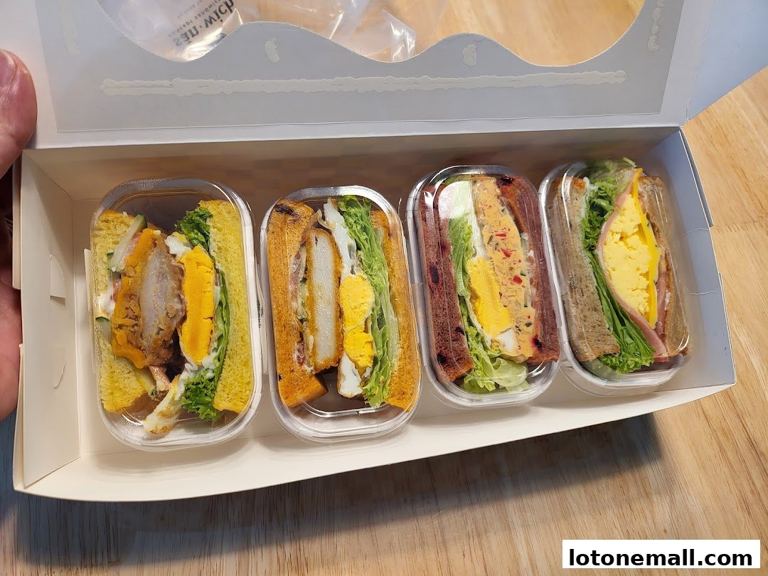 A box of four individually packaged sandwiches with various fillings and ingredients.