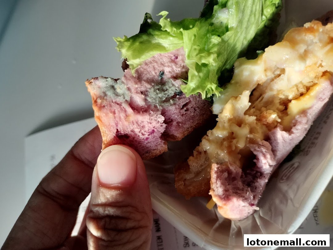 A hand holds a purple sandwich with lettuce and melted cheese filling.