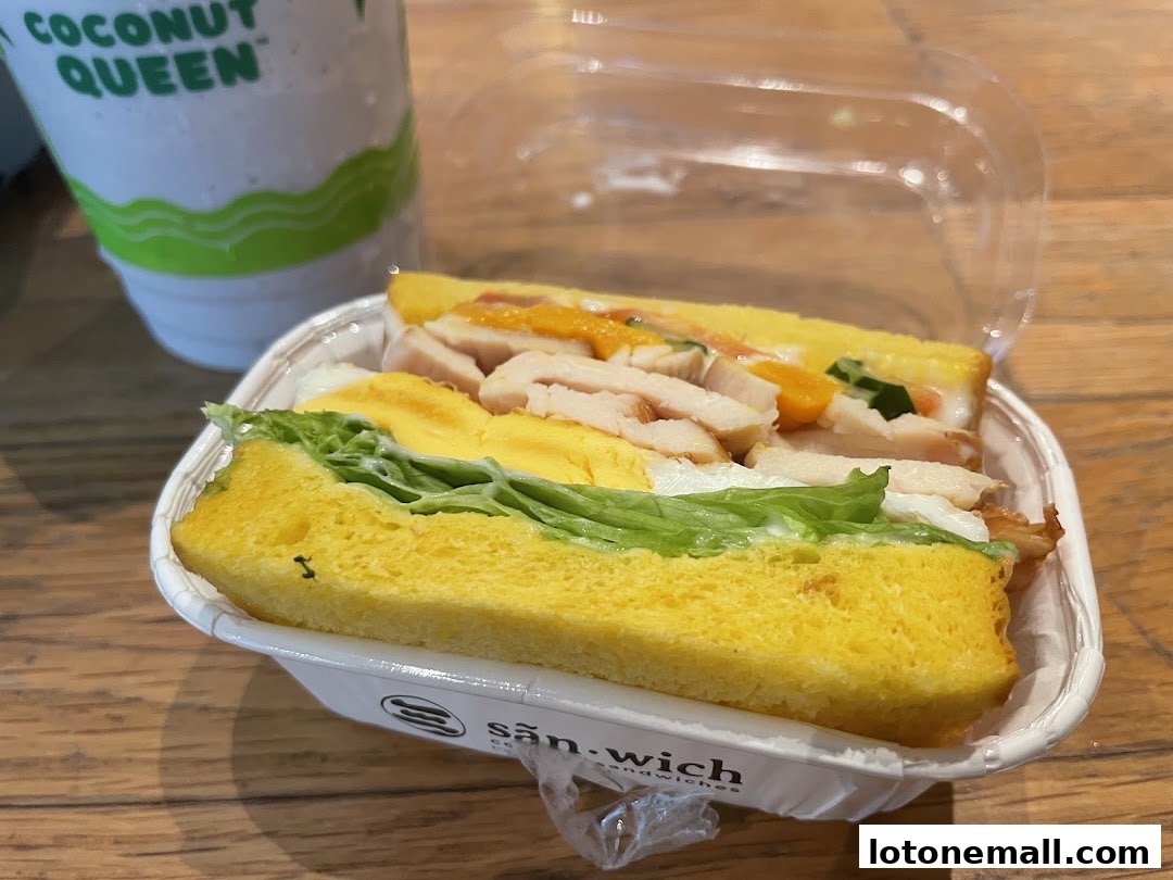 A delicious sandwich with chicken, egg, and lettuce, served in a takeaway container.
