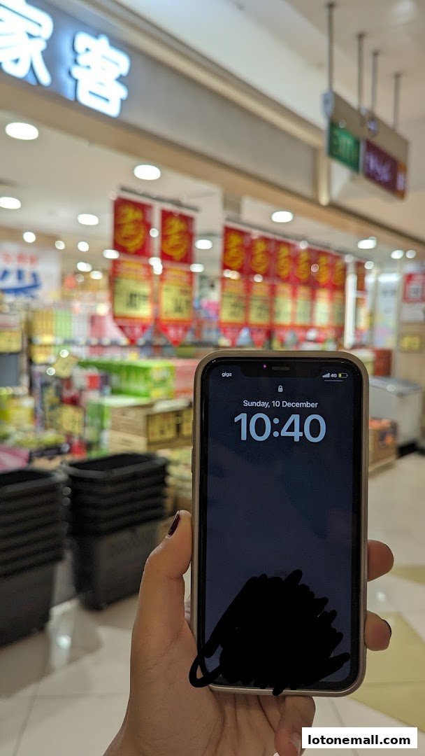 A person holds a smartphone in front of a supermarket interior with shelves of products.