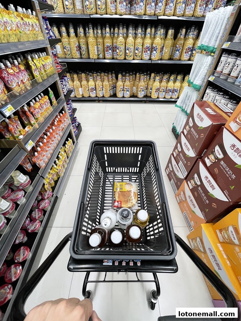 A shopping cart filled with drinks and snacks in a supermarket aisle.