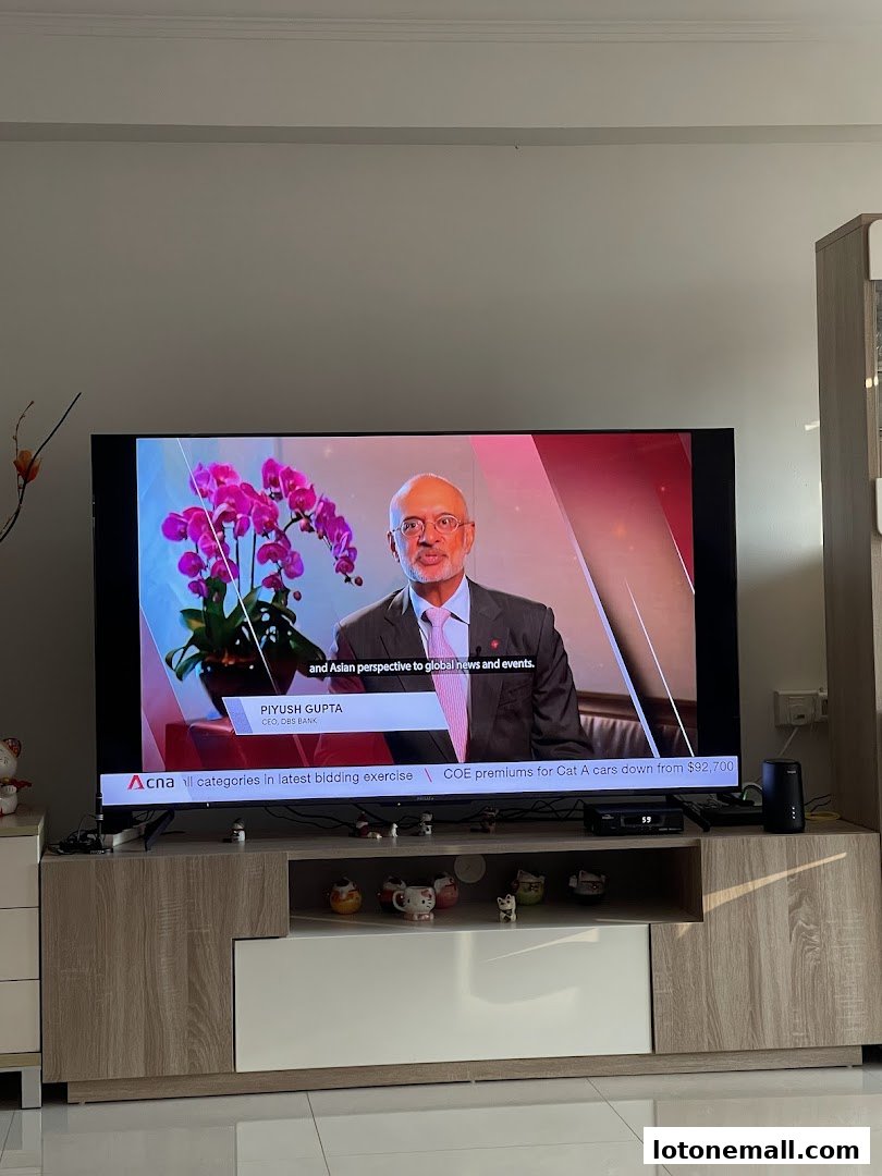A man in a suit speaks on a television screen next to pink orchids.