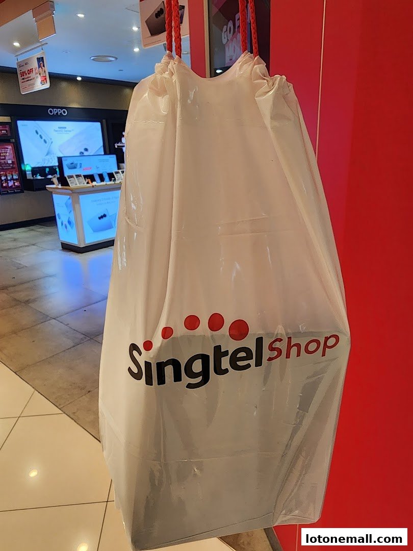 A white shopping bag with the Singtel logo hangs in front of a red wall.